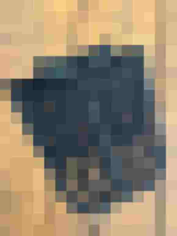 Schwarze Spitzen-Schürze mit Raffungen und Knöpfen auf einer Holzoberfläche.